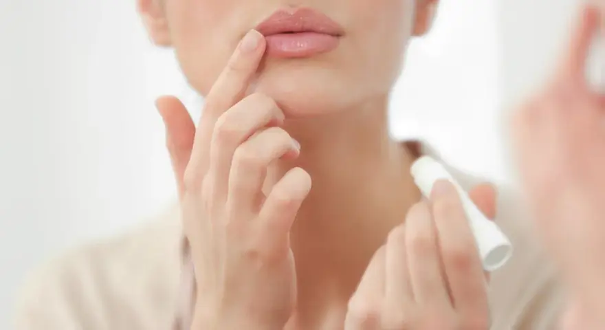 Una mujer aplica bálsamo labial, mostrando cómo son los labios perfectos: hidratados y suaves.