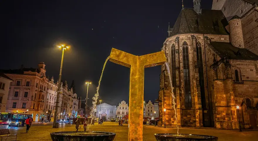 Złota fontanna w centrum miasta, obok zabytkowego kościoła. Wieczorne Pilzno, pełne urokliwych atrakcji.