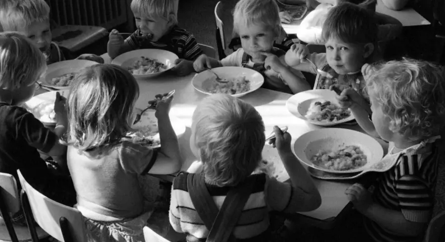 Kinder essen gemeinsam Brei. Ein Junge isst genüsslich, ein anderes Kind schaut nachdenklich. Erinnerungen an Kindheits Eis.