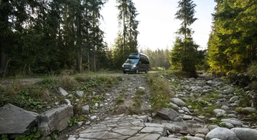 Kamper w górskiej scenerii Szwajcarii, na kamienistej drodze wśród świerków.