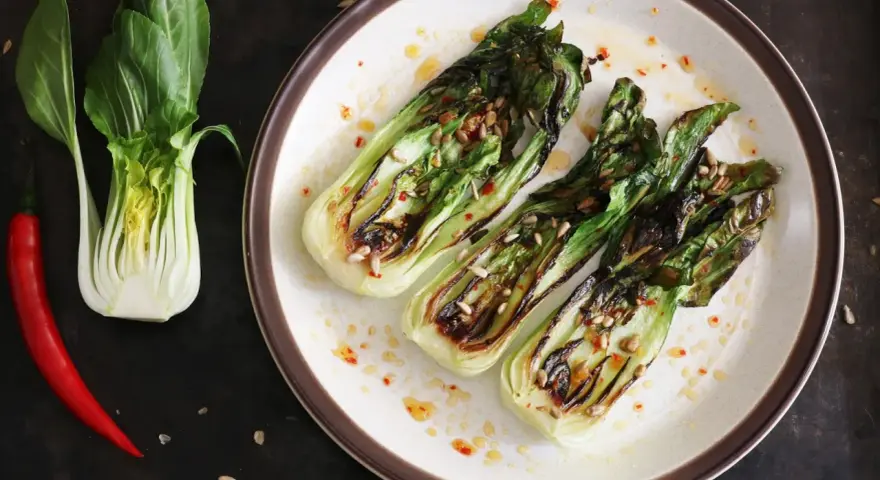Grillowany pak choi z nasionami słonecznika i papryczką chili na talerzu.