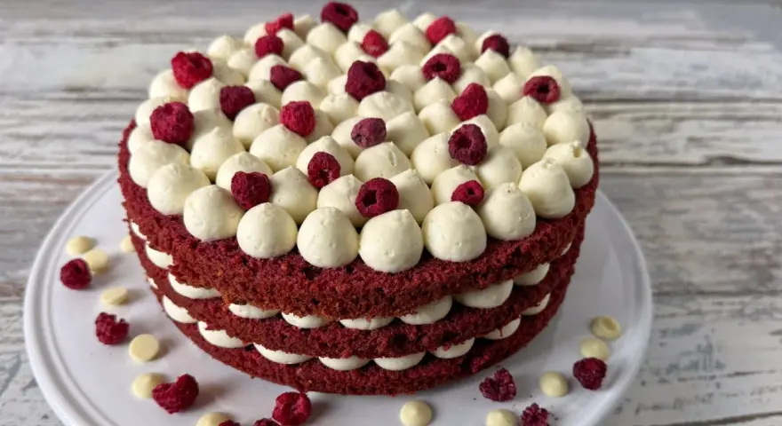 Ein mehrschichtiger Red Velvet Kuchen mit weißer Creme und Himbeeren.