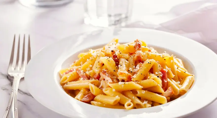 Piatto di pasta penne con speck e zafferano, guarnito con parmigiano e pepe nero.
