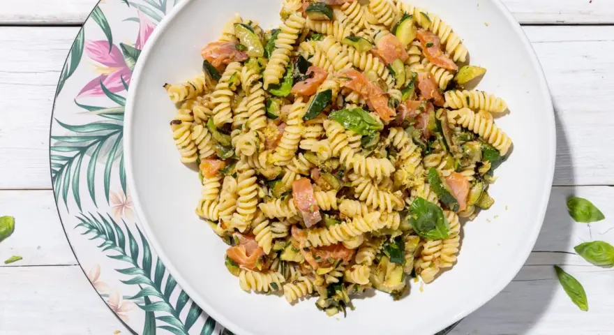 Un piatto invitante di pasta fredda con zucchine e salmone, condita con basilico fresco. Perfetta per un pasto estivo leggero e gustoso.