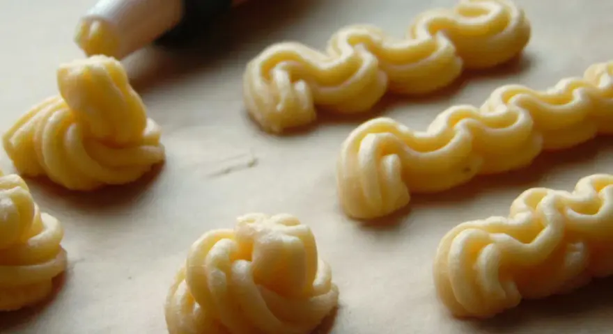 Kremowe eklery z czekoladą i profiteroles w trakcie przygotowania. Widać rękaw cukierniczy i wyciskane ciasto.