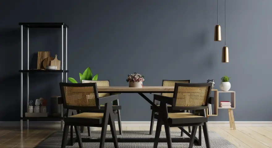Salle à manger moderne avec chaises en rotin et table en bois. Deux suspensions dorées au-dessus, une étagère noire à gauche. Idées pour comment éclairer une pièce sombre.