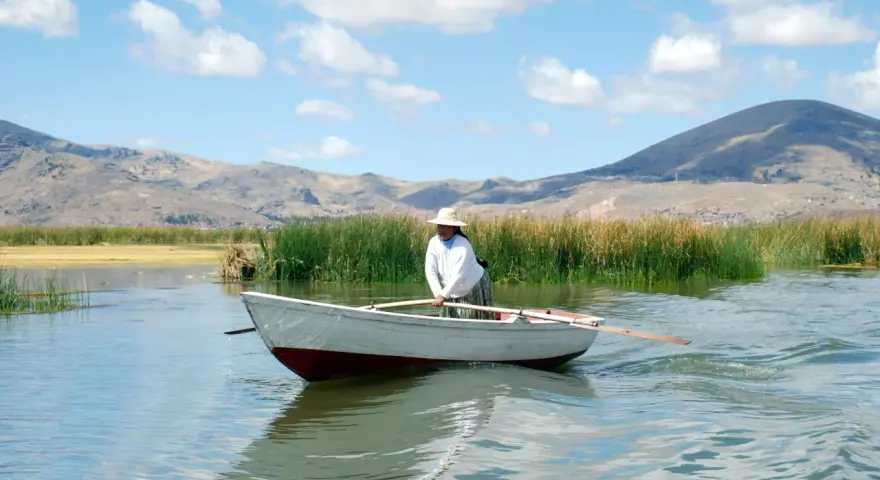 Donna con cappello di paglia rema su un lago, con montagne sullo sfondo. Mete agosto fuori Europa, un'immagine di pace.