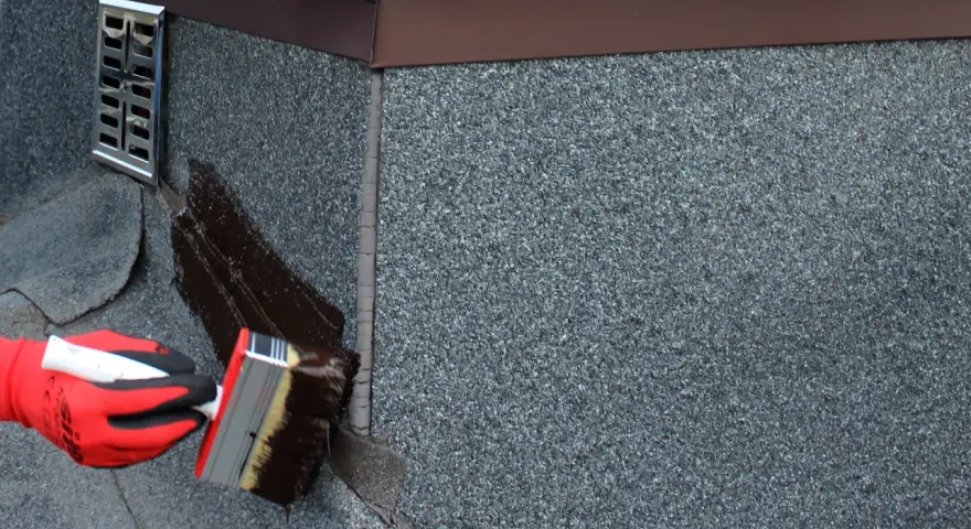 Rękawica w czerwonej rękawicy nakłada ciemną masę uszczelniającą, by disprobit zapobiec przeciekom.