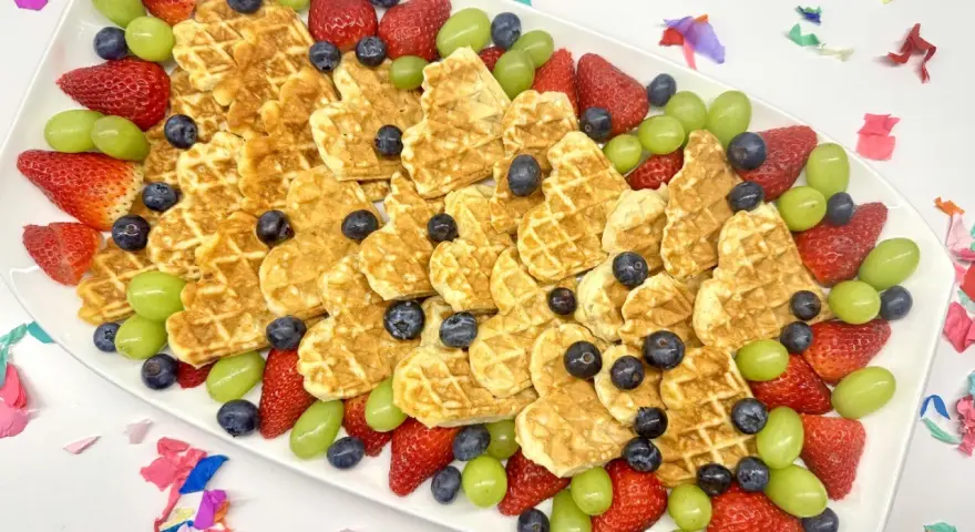 Herzförmige Waffeln mit Erdbeeren, Blaubeeren und grünen Trauben auf einem Teller – ein bunter obstteller kinder für jeden Anlass.