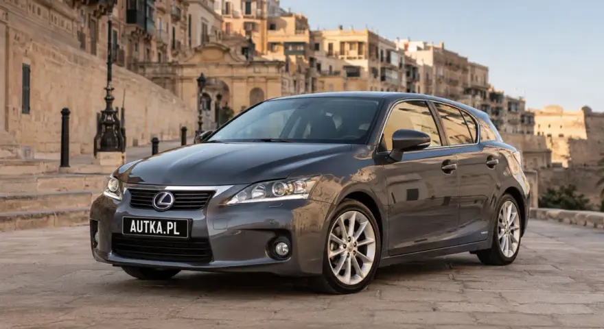 Szary Lexus CT 200h zaparkowany na brukowanej uliczce z zabytkowymi budynkami w tle.