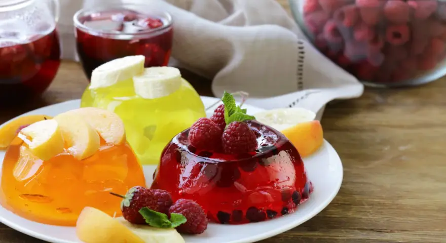 Tre colorate gelatine per dolci, guarnite con frutta fresca, invitano a un assaggio rinfrescante.