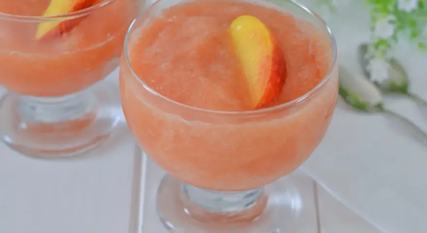 Coppa di granita alla pesca, rinfrescante e dolce, guarnita con una fetta di pesca fresca. Perfetta per un'estate golosa.
