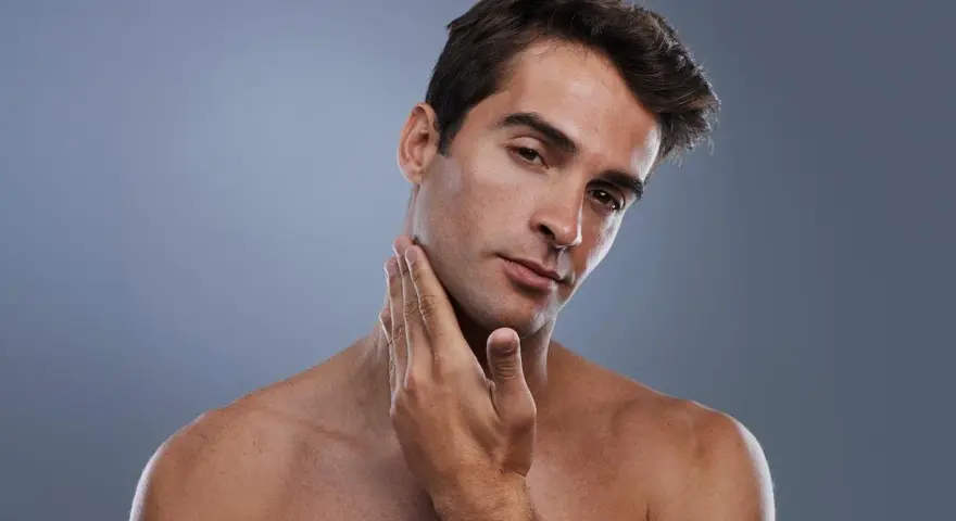 Hombre joven con piel suave y un afeitado perfecto, tocando su mandíbula con la mano.
