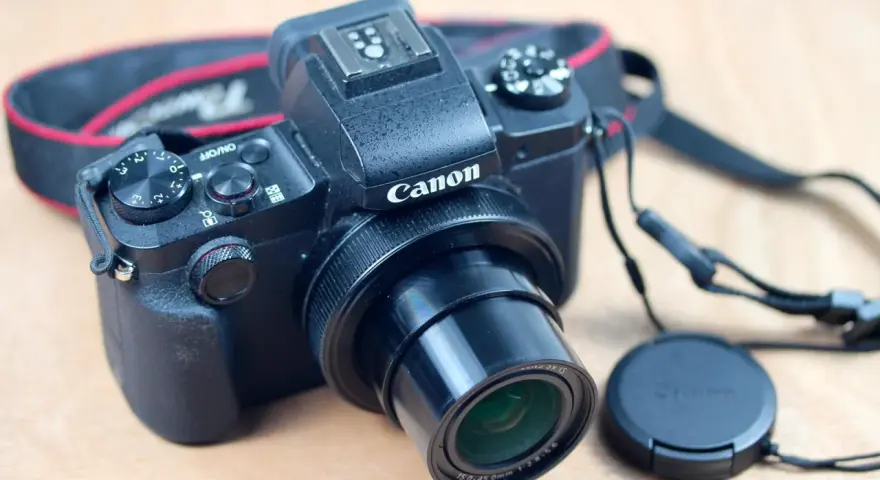 Un appareil photo noir Canon G1X Mark III, prêt pour un test. Courroie rouge et noire visible.