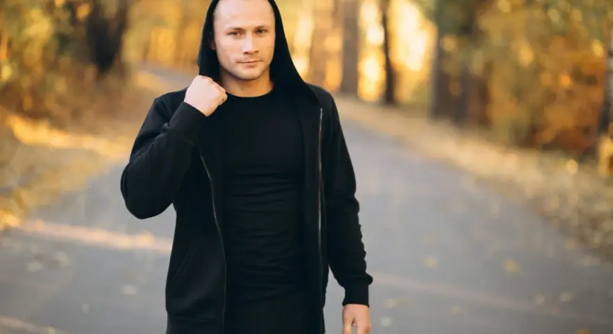 Mężczyzna w czarnej bluzie męskiej Guess z kapturem, stojący na ścieżce w jesiennym parku.