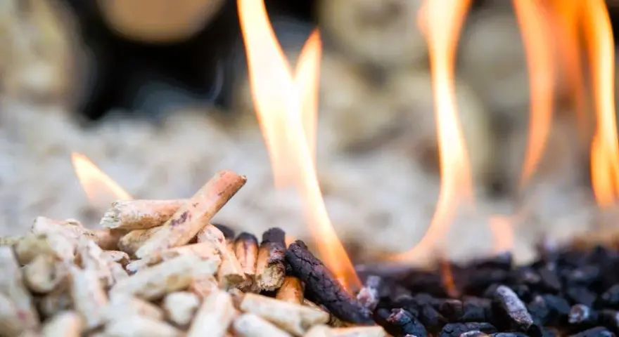 Fiamme danzano su pellet in combustione, un primo piano che mostra il passaggio dal legno chiaro alla cenere scura.
