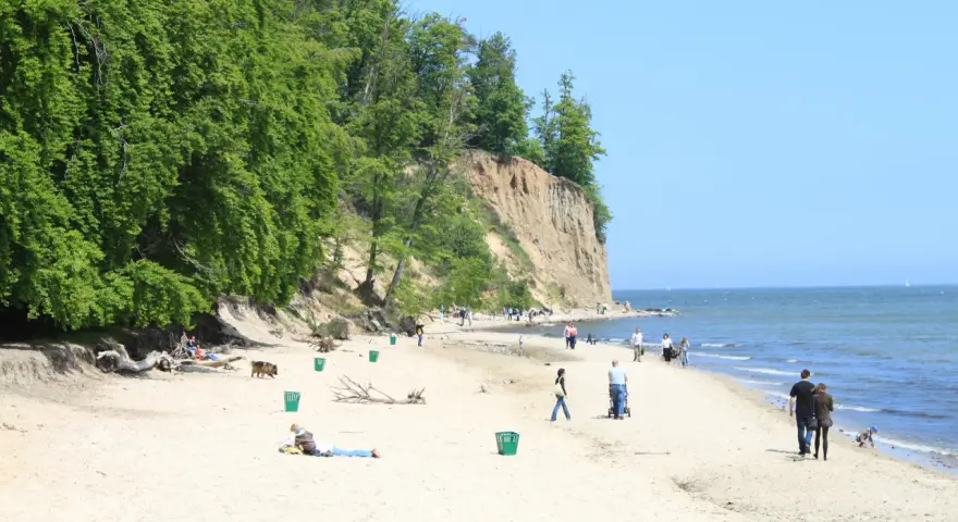 Słoneczny dzień na plaży przy klifie orłowskim. Ludzie spacerują, odpoczywają, a morze spokojnie faluje.