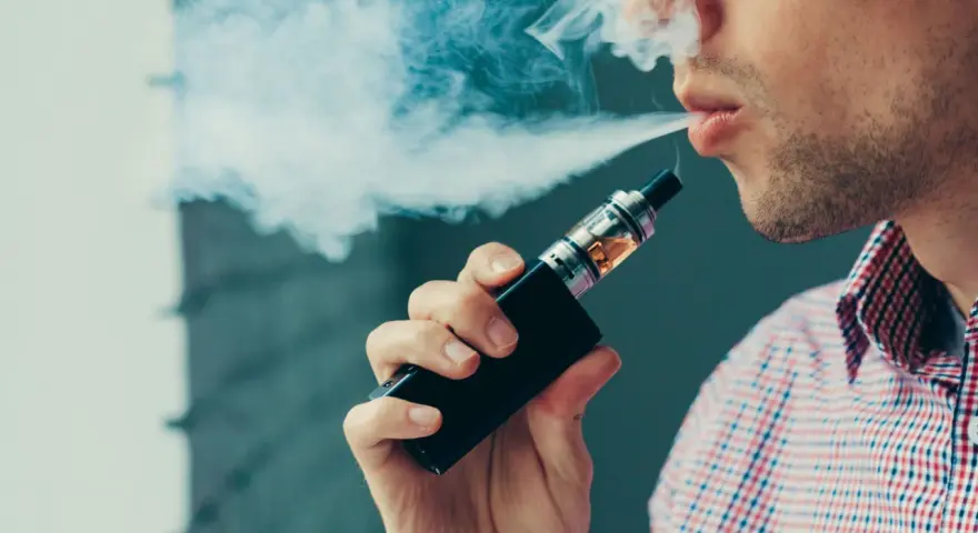 Hombre vapeando, exhala humo blanco. El vapear sube la tensión, cuidado con tu salud.