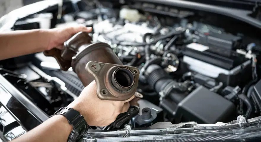 Mechanic holding a catalytic converter, ready for replacement. Understanding the catalytic converter replacement cost is key for car owners.