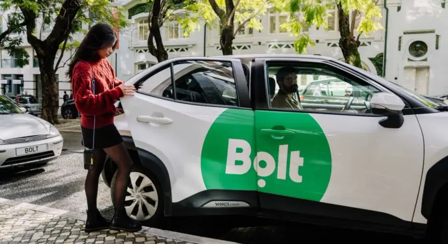 Junge Frau öffnet Tür eines weißen Bolt-Taxis. Fahrer wartet.
