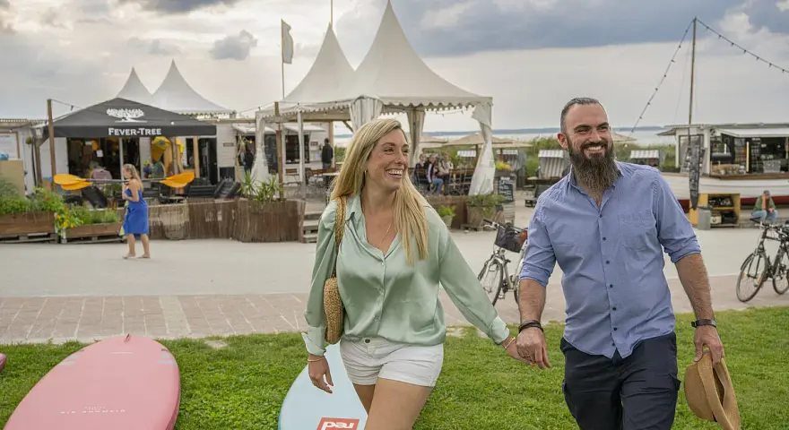 Glückliches Paar spaziert am **Stein Ostsee Strand** entlang, vorbei an SUP-Boards und Strandbuden.