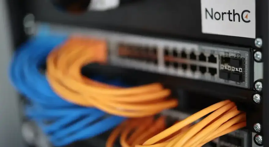 Netzwerkschrank mit blauen und orangen Kabeln, die an einen Switch angeschlossen sind.