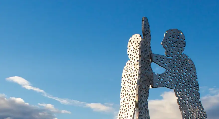 Der Molecule Man in Berlin, eine Skulptur aus Metall mit vielen Löchern, ragt gegen einen blauen Himmel mit Wolken.