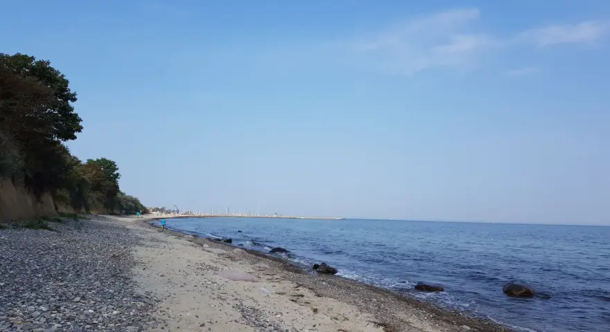 Ein ruhiger Tag am Wittenbeck Strand. Kies und Sand treffen auf das sanfte Meer, im Hintergrund eine Marina.