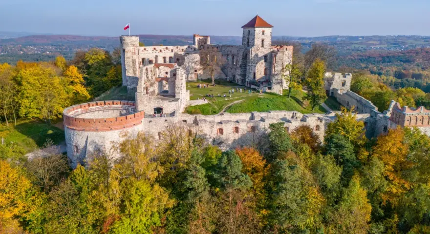Ruiny zamku na wzgórzu, część szlaku Orlich Gniazd. Jesienne drzewa otaczają kamienne mury.