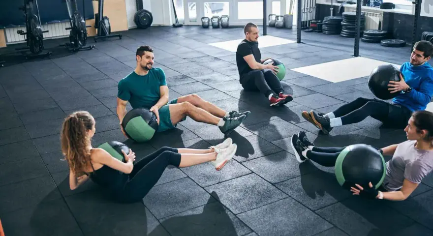 Fünf Personen machen im Fitnessstudio Sit-ups mit Medizinbällen.
