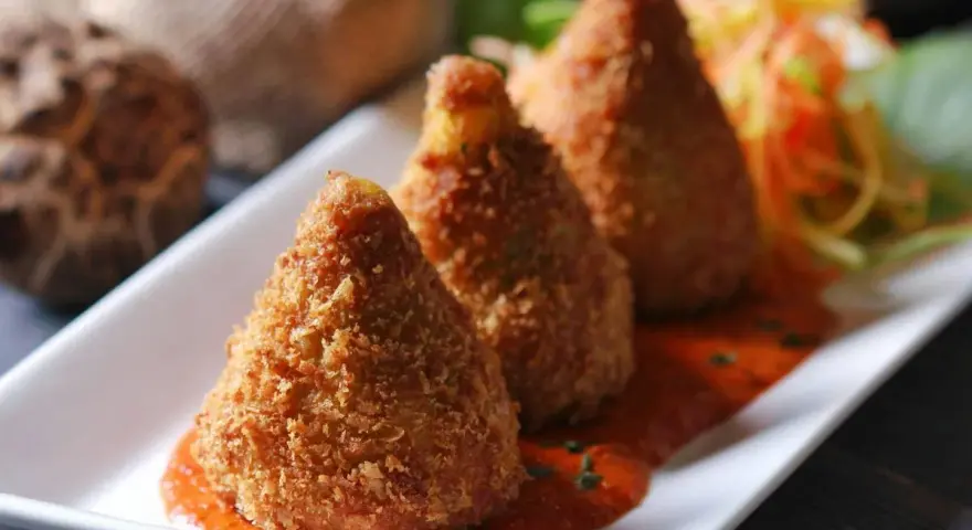 Złociste arancini, idealne do domowego arancini przepis, podane na talerzu z sosem pomidorowym i surówką.