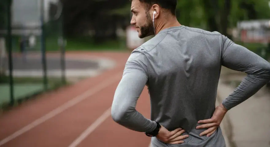 Uomo con le mani sulla schiena, che indica dolore. Forse correre fa male alla schiena, o forse è solo un momento di pausa.