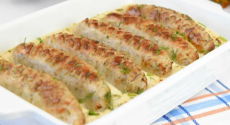 Aromaticzna biała kiełbasa w sosie chrzanowo-musztardowym, udekorowana świeżym koperkiem, podana w białej zapiekance.