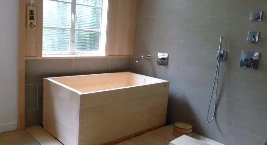 Un baño japonés con tina de madera, ducha y un pequeño taburete. El letrero de madera indica "男湯" (baño de hombres).
