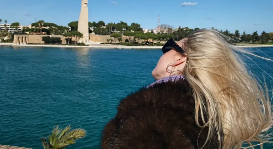Kobieta z blond włosami podziwia pomnik i morze w Brindisi. Warto zobaczyć to miejsce!
