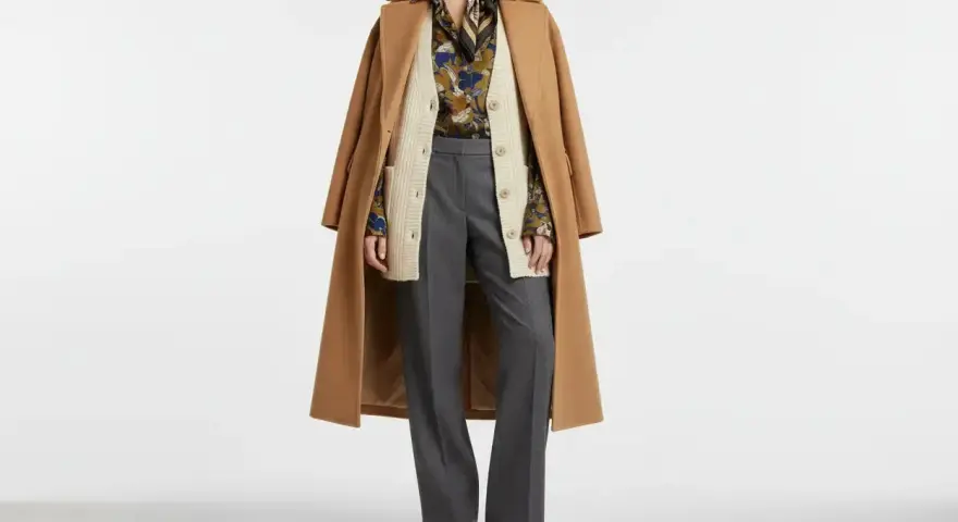 Modello con cappotto cammello, cardigan beige, camicia fantasia, pantaloni grigi e scarpe marroni. Un esempio di vestirsi a cipolla significato per adattarsi a ogni temperatura.