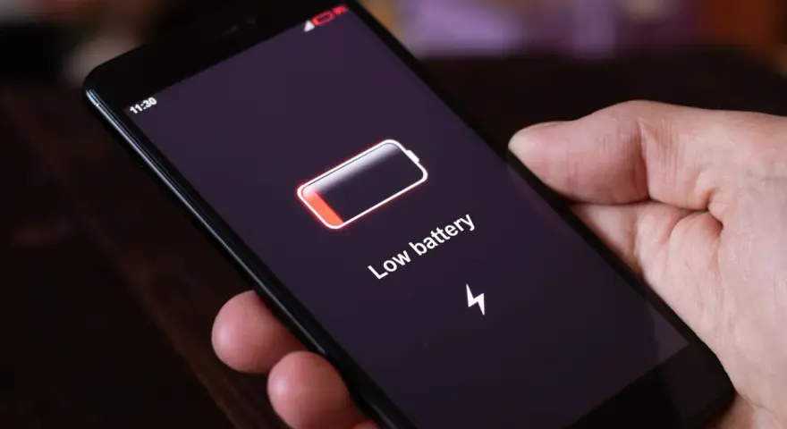 Dłoń trzyma smartfon z komunikatem "Low battery". Czas na naukę, jak oszczędzać baterię w telefonie, by uniknąć takich sytuacji.