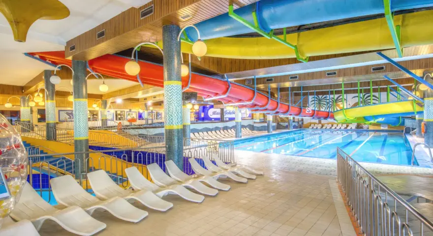 Kolorowy basen w Hotelu Gołębiowski z rynnami zjeżdżalni, leżakami i wodą.