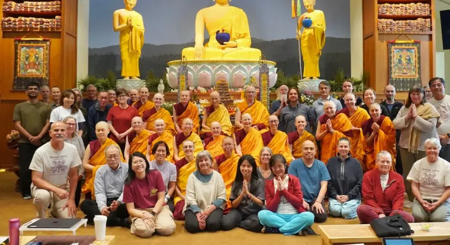 A large group of monks and laypeople gather for a photo in front of a golden Buddha statue, celebrating their shared religion.