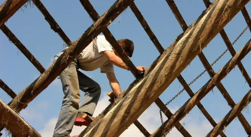 Mężczyzna pracuje na drewnianej konstrukcji dachu pod błękitnym niebem.