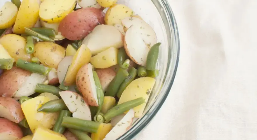 Insalata colorata di fagiolini e patate novelle, condita con erbe aromatiche, in una ciotola di vetro.