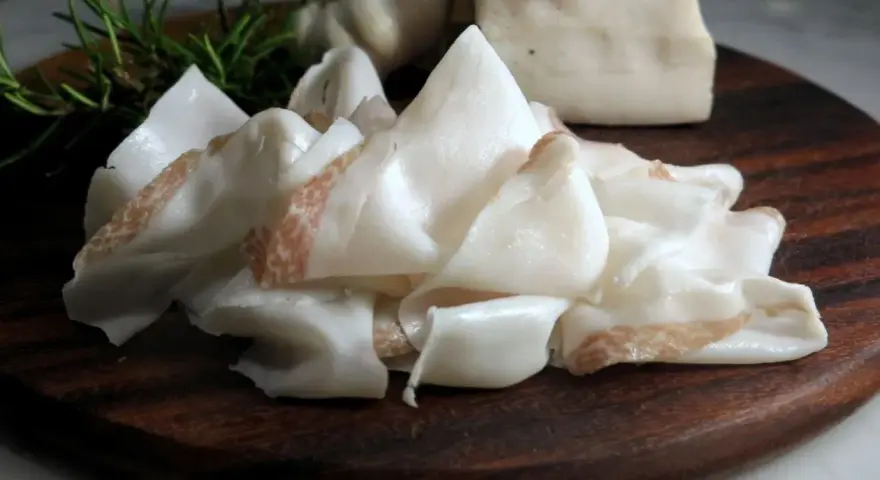 Fette sottili di lardo di Colonnata, profumate con rosmarino e aglio, pronte per essere gustate.