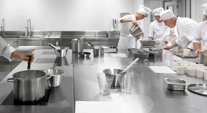 Estudiantes de cocina aprenden sobre seguridad en la cocina, preparando ingredientes en una estación de acero inoxidable.