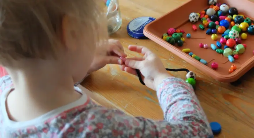 Dziecko uczy się, jak nawlec koraliki na sznurek, tworząc kolorową biżuterię.