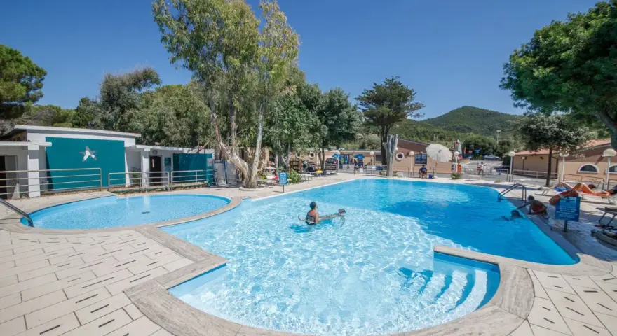 Dzieci pluskają się w basenie na terenie Miramare Camping Village. Słoneczny dzień, błękitne niebo i zieleń drzew tworzą wakacyjny klimat.