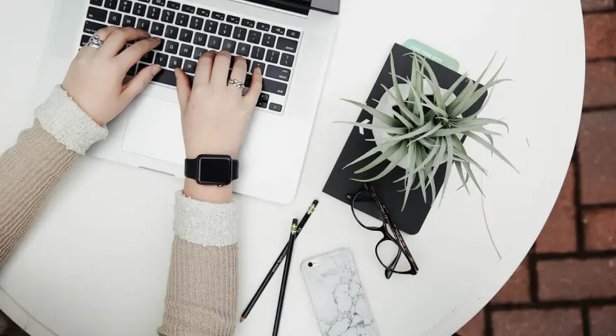 Kobieta pracuje na laptopie, obok leżą okulary, telefon i roślina. To idealne zdjęcia w chmurze do inspiracji.