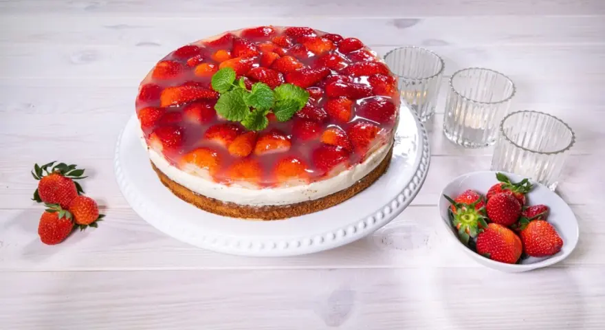 Eine köstliche Erdbeer Joghurt Sahne Torte, bedeckt mit frischen Erdbeeren und Tortenguss, garniert mit Minze.