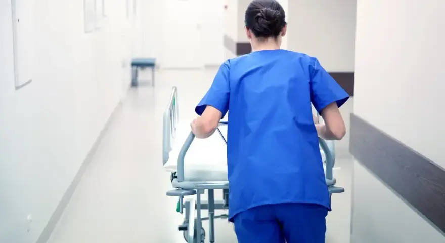 Salowa w niebieskim uniformie pcha łóżko szpitalne korytarzem. To część jej obowiązków w szpitalu.