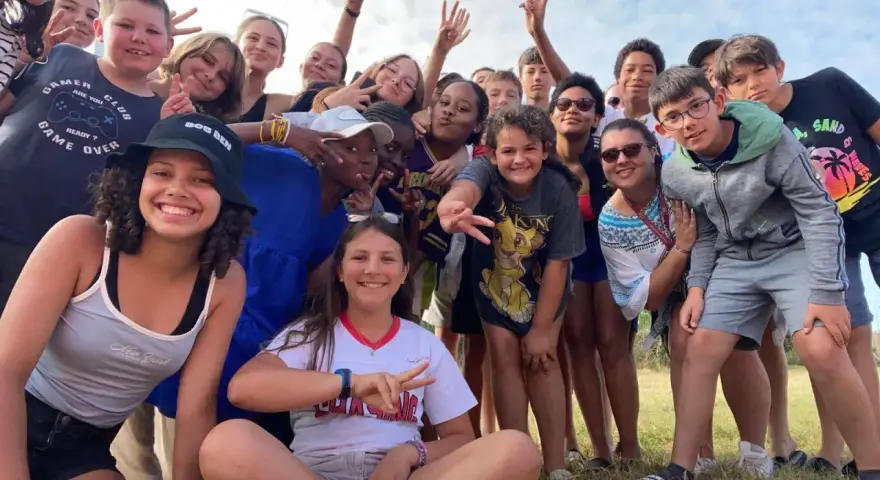 Un groupe d'enfants souriants fait un selfie en plein air, certains faisant le signe de paix.