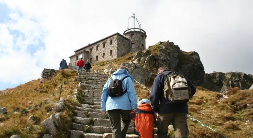 Rodzina wspina się kamiennymi schodami na Kasprowy Wierch. Na szczycie widać budynek obserwatorium.